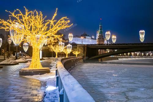 Фотография запечатлевает заснеженную Кремлевскую набережную, украшенную новогодней иллюминацией. 
Фото подходит для использования в тематических материалах о зимних праздниках в России, в туристических брошюрах и презентациях о Москве. Оно также может стать привлекательным элементом декора для праздничных открыток.