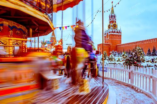 На фотографии представлена новогодняя карусель на Красной площади в Москве. Посетители, весело кружащиеся на фоне Кремля, создают атмосферу веселья и радости новогодних праздников. Этот кадр подходит для использования в рекламе новогодних мероприятий в Москве, привлекая внимание тех, кто ищет уникальные впечатления во время новогодних праздников. Фотография иллюстрирует теплую атмосферу зимнего волшебства у исторических зданий Красной площади.