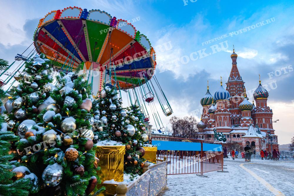 На фотографии изображена праздничная зимняя сцена в Москве, где перед Собором Василия Блаженного установлены новогодние украшения и аттракцион. Фотография подходит для использования в туристических брошюрах, праздничных публикациях, статьях о культурных традициях России или в качестве открытки для поздравлений с Рождеством и Новым годом.