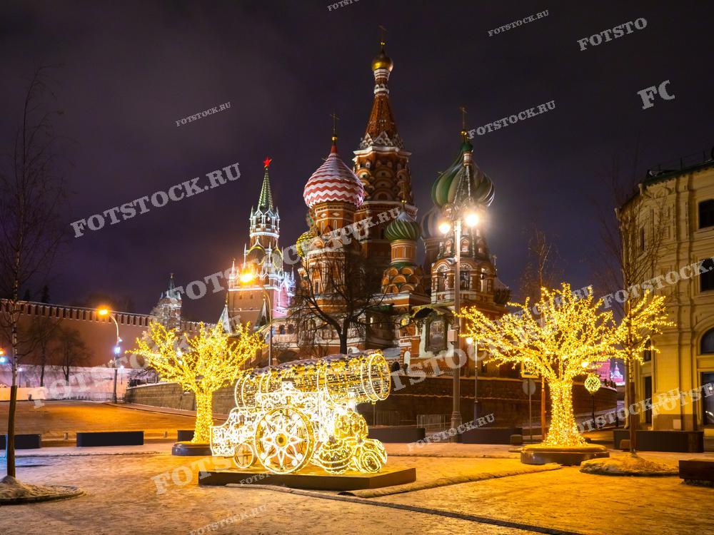 На фотографии изображена Красная площадь ночью зимой. В центре кадра виден Собор Василия Блаженного, окруженный праздничной иллюминацией и светящимися украшениями. Декоративные светящиеся деревья и арт-объекты создают волшебную атмосферу.