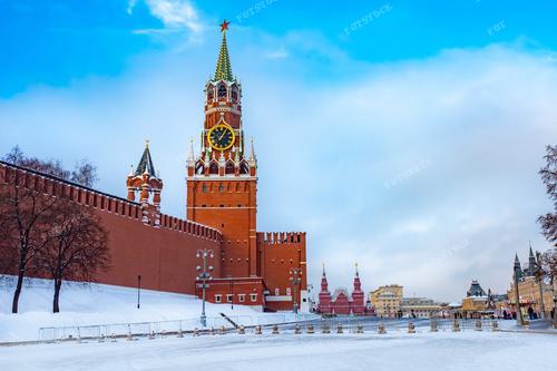 Величественная зимняя панорама Московского Кремля, запечатлевшая красоту Спасской башни с курантами и звездой на шпиле. 
Архитектурные шедевры города, представленные на фотографии, включают уникальные элементы московской архитектуры. Этот кадр подчеркивает важность российских городов и символизирует культурное наследие. Изумительная панорама станет отличным дополнением к изданиям о Москве, историческим статьям и географическим публикациям.