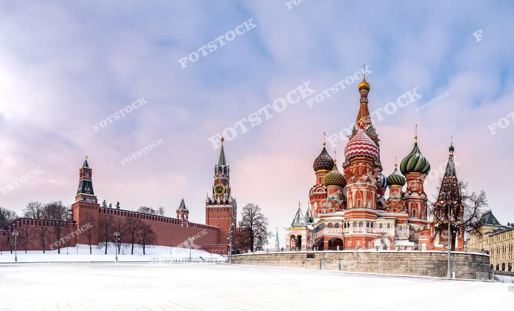 На фотографии запечатлен Собор Василия Блаженного на Красной площади в Москве, окруженный заснеженным ландшафтом. На заднем плане видна часть Кремлевской стены и Спасская башня с курантами.