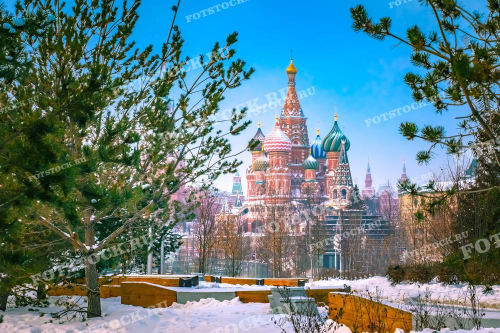 На фото изображен собор Василия Блаженного в Москве, видимый через деревья, покрытые снегом. Зимняя атмосфера подчеркивает красоту исторического памятника. Фотография подходит для использования в туристических путеводителях, открытках и рекламных материалах, посвященных зимней Москве.