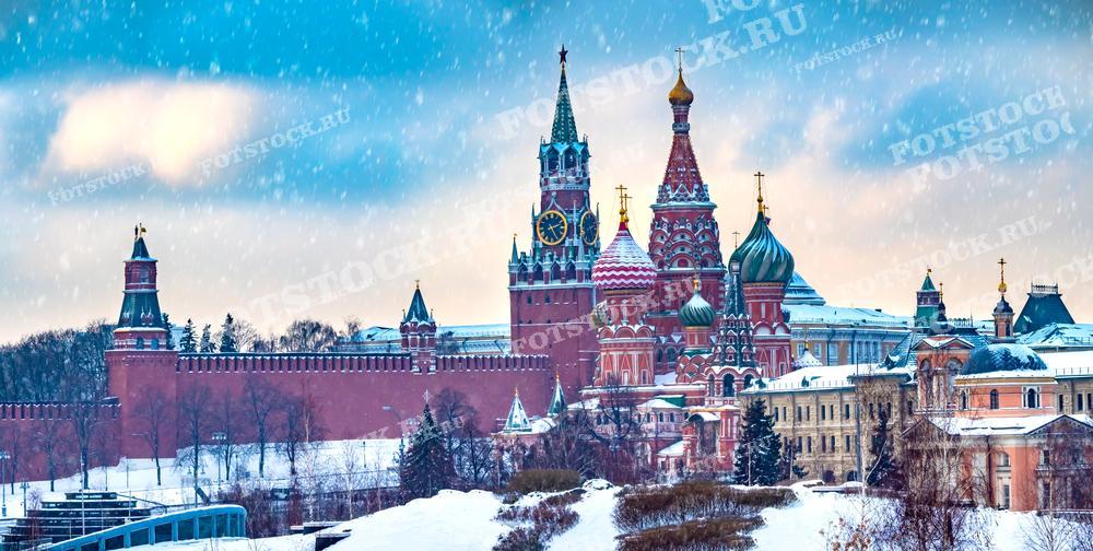На фотографии изображен зимний вид на Московский Кремль и Собор Василия Блаженного. Снегопад добавляет этому знаменитому архитектурному ансамблю особенно торжественный и почти сказочный вид. Кремлевские стены и башни, увенчанные звёздами, а также яркие купола собора являются символами российской истории и культуры. Это изображение прекрасно подходит для использования в туристических публикациях, исторических книгах, образовательных материалах и статьях о российской культуре и архитектуре.