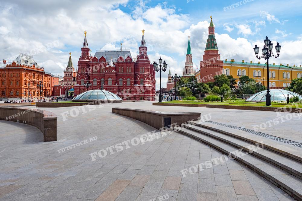 На фотографии изображен вид на Красную площадь в Москве, с Историческим музеем на переднем плане и Спасской башней Кремля на заднем. Это дневной снимок, демонстрирующий архитектурные достопримечательности столицы. Фотография подходит для использования в туристических буклетах, статьях о Москве и иллюстрациях об исторических местах города.