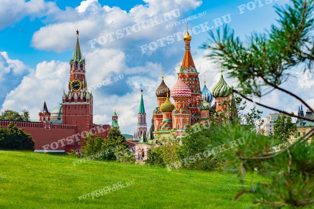 На фотографии изображён вид на Красную площадь в Москве. На переднем плане зелёный газон и деревья, а на заднем плане — иконичные архитектурные сооружения: Собор Василия Блаженного и Спасская башня Кремля. Эта композиция подчеркивает красоту и величие московских достопримечательностей в сочетании с природной зеленью. Фотография отлично подойдет для использования в путеводителях, туристических брошюрах, культурно-исторических изданиях, а также как декоративный элемент в оформлении помещений или веб-сайтов, связанных с российской культурой и туризмом.