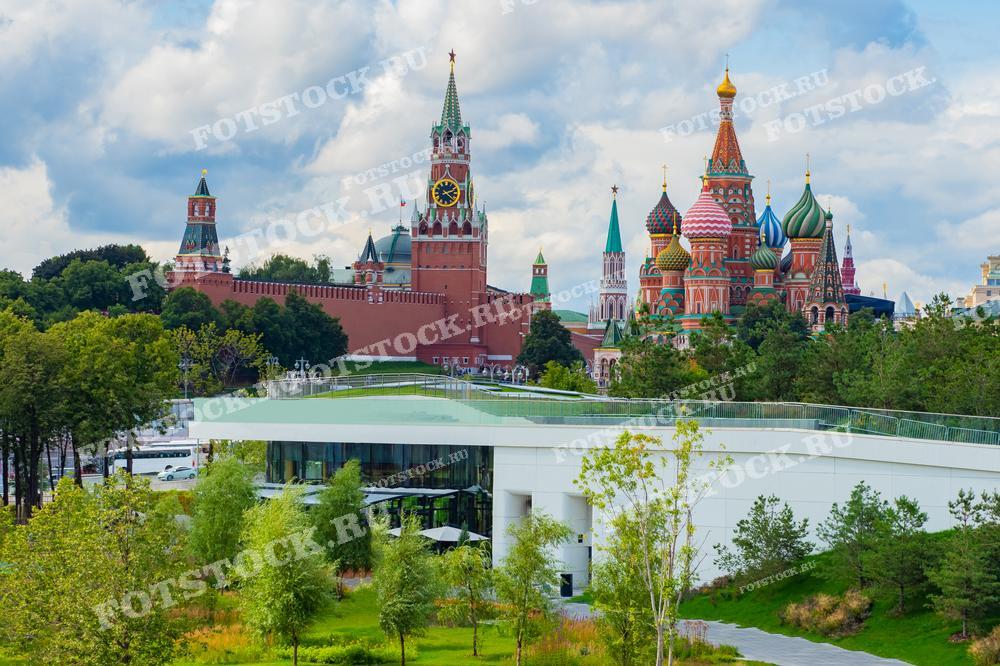 На фотографии изображен вид на Кремль и Собор Василия Блаженного из Парка Зарядье в Москве. Летний день, зелень парка контрастирует с красными стенами Кремля и яркими куполами собора. Фотография идеально подходит для туристических буклетов, статей о Москве и иллюстраций об исторических и современных достопримечательностях столицы.