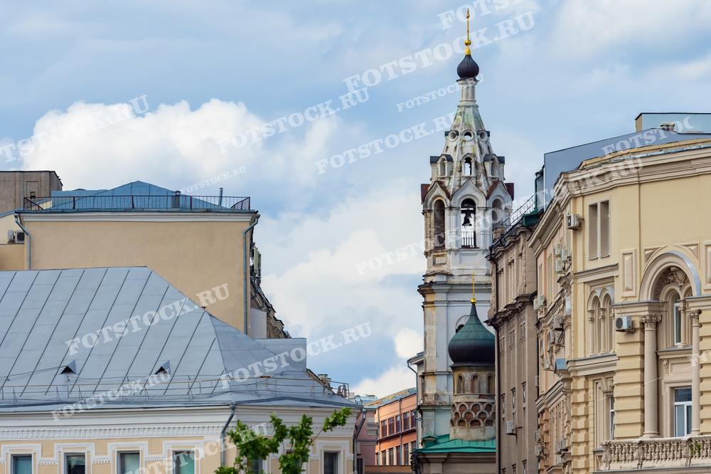 На фотографии запечатлены архитектурные детали старинных зданий в Москве. Видны элементы классической архитектуры: сложные карнизы, декоративные оконные рамы и характерная для русской архитектуры церковная башня с луковичной куполом. Этот снимок иллюстрирует архитектурное разнообразие и историческое наследие Москвы, делая его идеальным для использования в культурных публикациях, исторических исследованиях и архитектурных обзорах.
