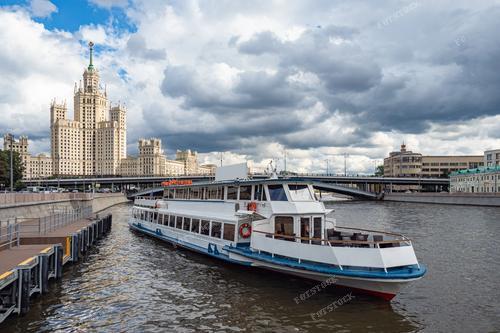 Плавное отправление туристического судна с московской пристани отмечает начало увлекательного водного тура по столице. На заднем плане величественное высотное здание в центре города создает красивый контраст с прибрежной идиллией. Фотография идеально подходит для иллюстрации путеводителей, рекламы водных экскурсий и статей о туристических достопримечательностях Москвы. Облачный день придает снимку умиротворенность и приглашает зрителя присоединиться к путешествию.