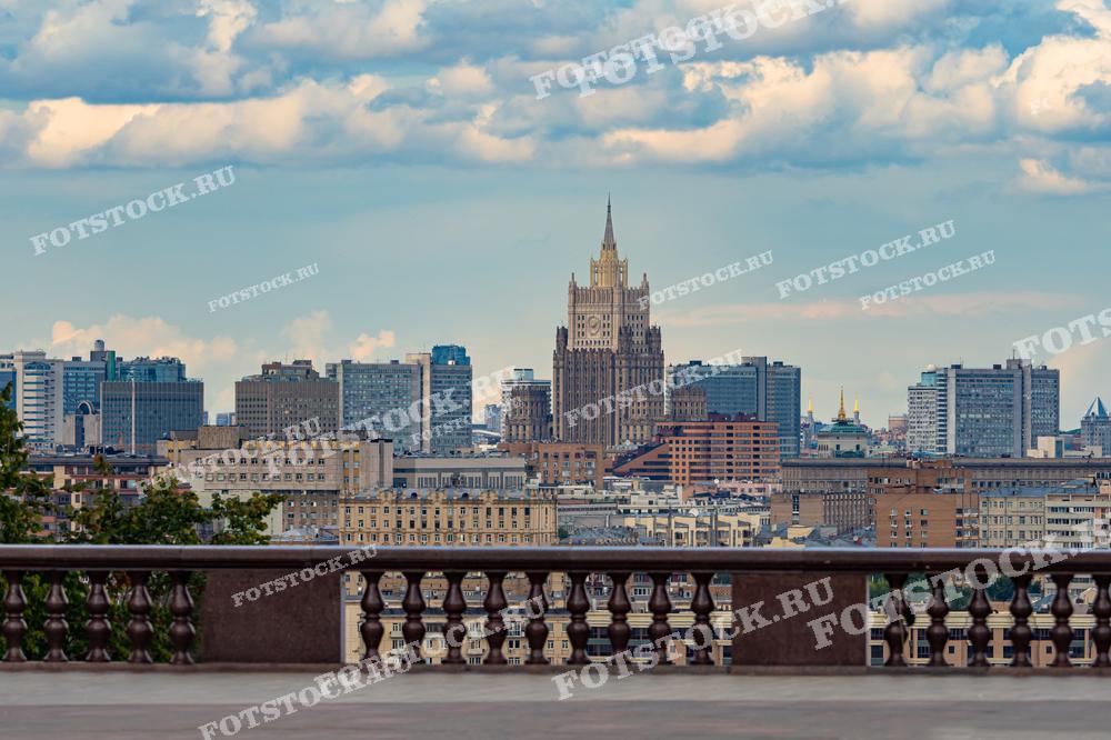 На фотографии представлен вид на Москву с обзорной площадки, с которой открывается панорама города. В центре кадра возвышается одно из семи сталинских высотных зданий — Министерство иностранных дел России, выделяющееся своим неоготическим стилем. Вокруг него расположены современные офисные и жилые здания.