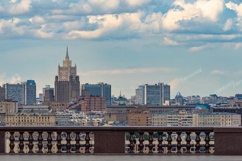 На фотографии представлен стандартный урбанистический пейзаж столичного сердца – Москвы. Вид на здание Министерства иностранных дел России на фоне мраморного парапета создает атмосферу спокойствия и величественности. Серые оттенки подчеркивают строгость городского ландшафта. Фотография идеально вписывается в статьи о российской столице, официальных учреждениях и архитектурных элементах города.
