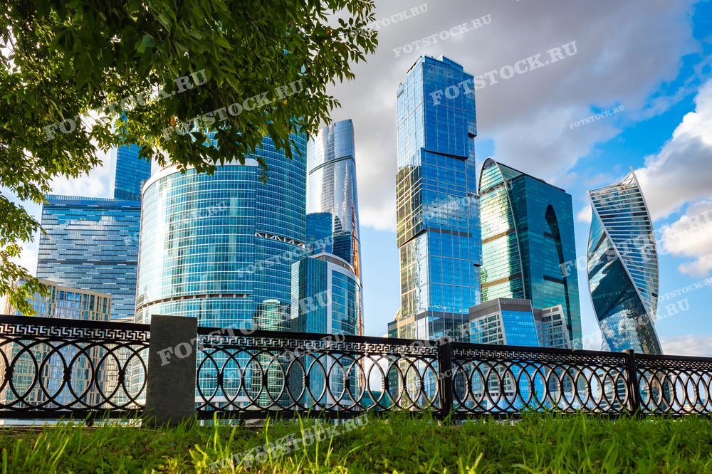 На фотографии представлен вид на деловой центр Москва-Сити, подчеркивающий контраст между современными небоскребами и традиционным ограждением из чугуна на переднем плане. Эта композиция иллюстрирует сочетание природы и урбанистики, делая изображение подходящим для обсуждения тем городского планирования, архитектуры и экологии в городских условиях. Фотография отлично подойдет для использования в презентациях, публикациях о современной архитектуре и туристических гидах по Москве.