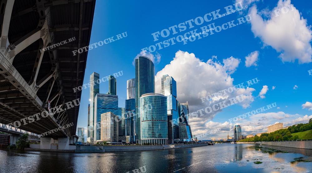 На фотографии представлен вид на деловой центр Москва-Сити, снятый из-под моста через Москву-реку. 
Фотография идеально подходит для использования в архитектурных журналах, туристических проспектах и образовательных материалах о развитии современных мегаполисов.