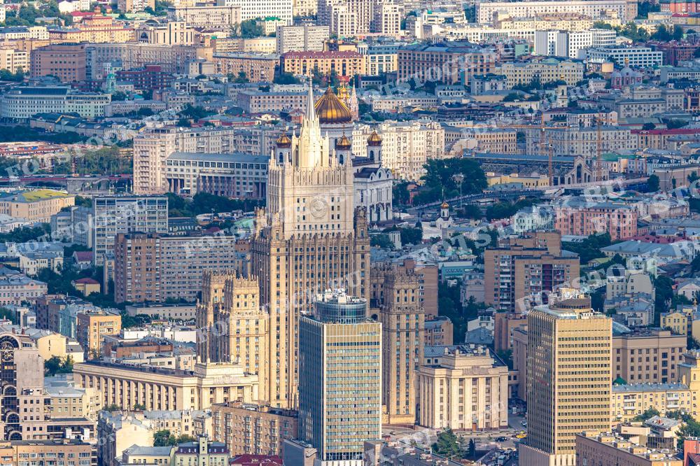 На фотографии изображен вид сверху на одну из сталинских высоток в Москве, окружённую разнообразной городской застройкой. Это изображение демонстрирует плотную урбанизацию столицы, где исторические здания соседствуют с современными офисными центрами. Фотография позволяет оценить масштабы и архитектурное разнообразие Москвы, что делает её подходящей для использования в статьях о городском планировании, истории архитектуры или культурных путеводителях.