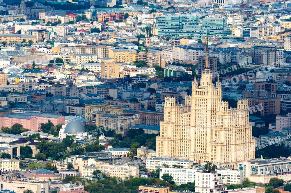 На фотографии представлена панорама центральной части Москвы с высоты птичьего полета. В центре внимания одна из знаменитых сталинских высоток — здание Министерства иностранных дел. Окружающий городской пейзаж разнообразен — можно увидеть как старинные здания, так и современные постройки. Летний день добавляет яркости и четкости деталям, делая вид города живым и динамичным. Такой ракурс позволяет оценить архитектурное разнообразие Москвы.