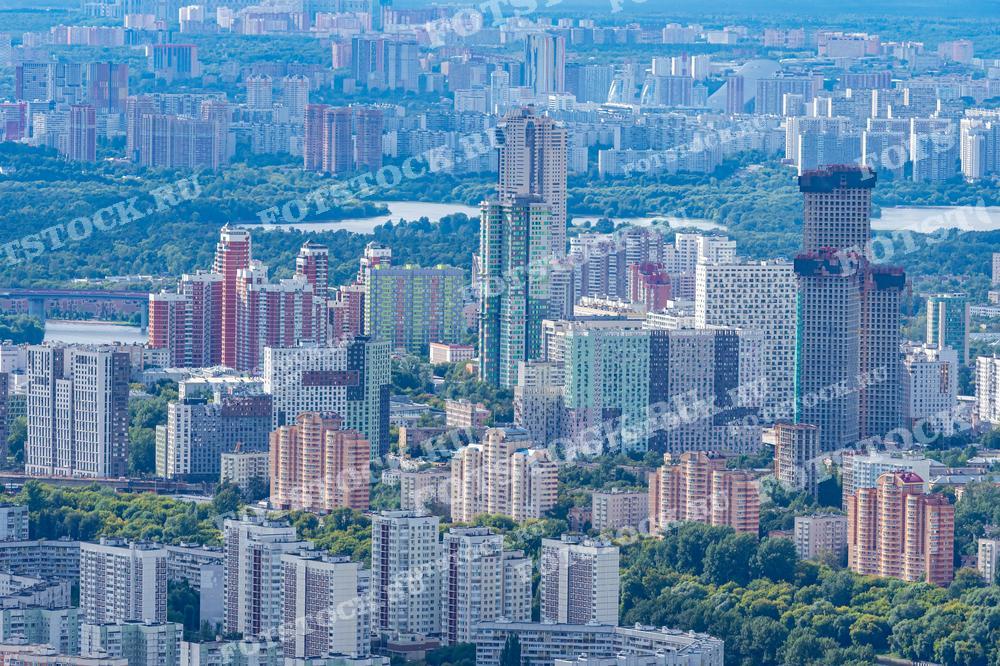 На фотографии представлен вид на различные районы Москвы, демонстрирующий плотную застройку города, включая множество высотных жилых комплексов, которые расположены на фоне обширных зелёных парковых зон. Этот снимок идеален для использования в исследованиях и публикациях, посвященных городскому планированию, архитектуре и урбанистике, а также в материалах, которые освещают жизнь в больших городах.