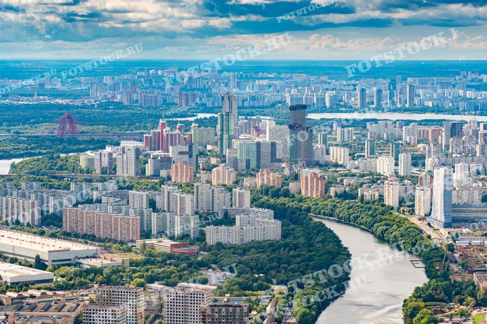 На фотографии изображена панорама Москвы с высоты, видно множество жилых и административных зданий, река Москва и живописный мост. Фото можно использовать для иллюстраций, рекламы и туристических материалов.