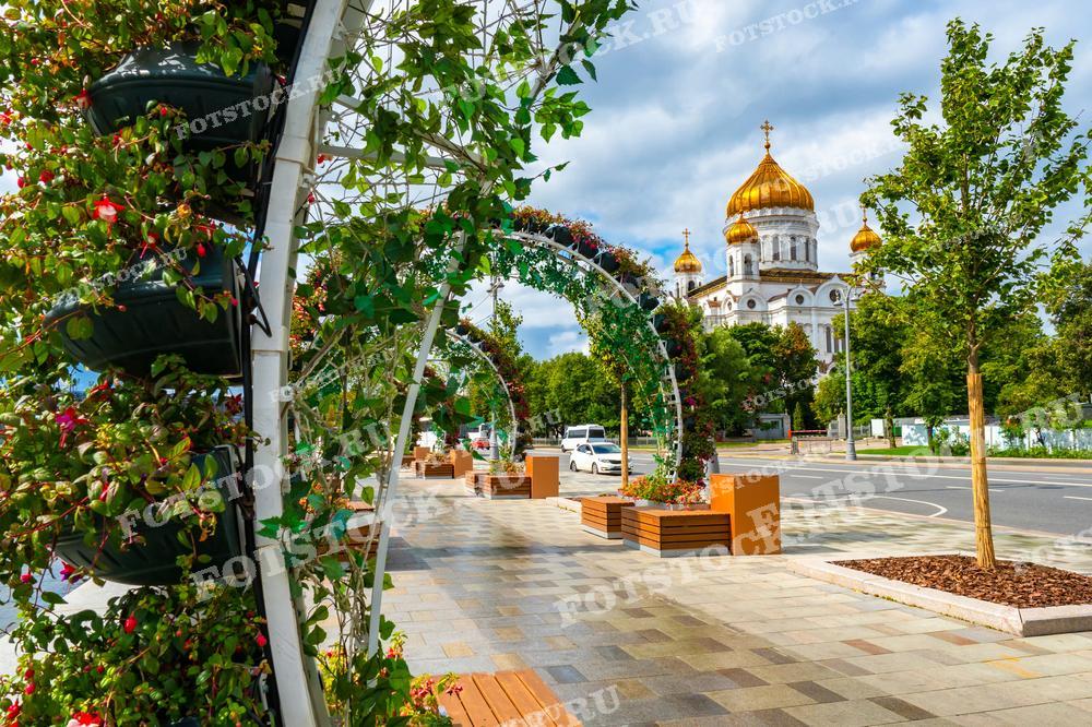 На фотографии изображена улица в Москве, украшенная цветочными арками, ведущая к Храму Христа Спасителя. 
Этот снимок может быть использован в туристических брошюрах, культурных и образовательных материалах, а также для украшения интерьеров или в качестве вдохновения для ландшафтных дизайнеров.