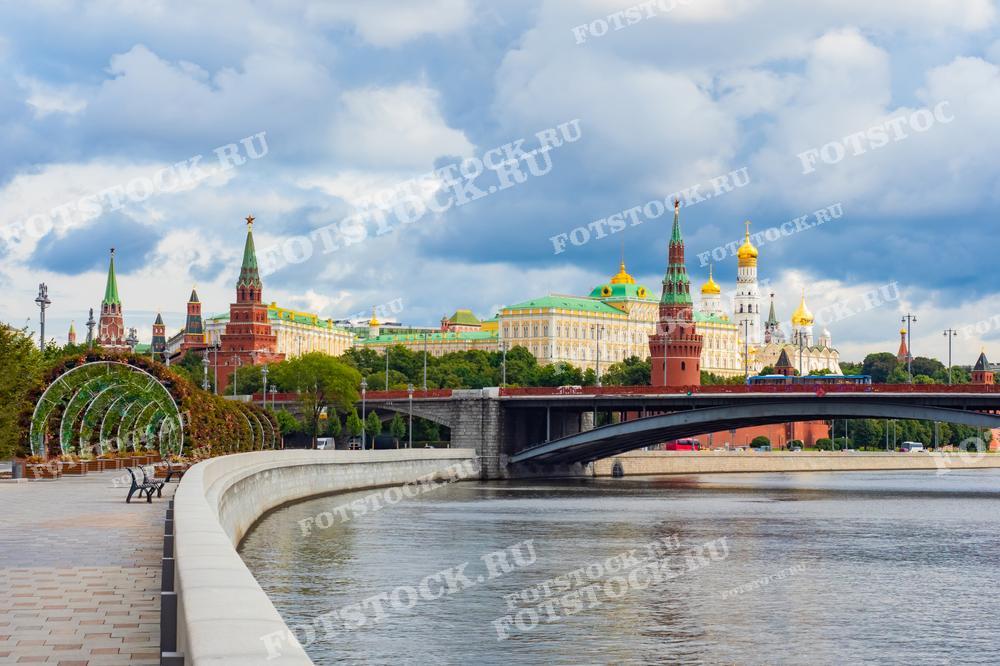 На фотографии изображен вид на Кремль и набережную Москвы-реки. Летний день и арки, украшенные цветами, подчеркивают красоту и архитектурное величие исторического центра Москвы.