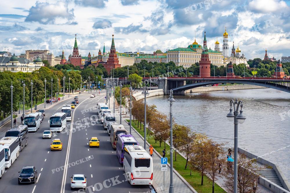 На фотографии изображены Кремль и Москва-река, вид с набережной. На переднем плане — автодорога с автомобилями и автобусами. Фото можно использовать для иллюстраций, рекламы и туристических материалов.