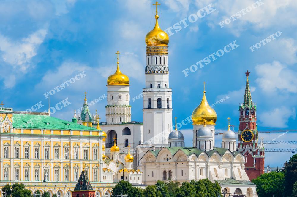 На фотографии запечатлены знаменитые достопримечательности Московского Кремля. В центре кадра расположена колокольня Ивана Великого, окружённая золотыми куполами соборов. Слева выделяется Большой Кремлёвский дворец с зелёной крышей и изящным декором. Справа видна Спасская башня с часами, являющаяся одним из символов Москвы.