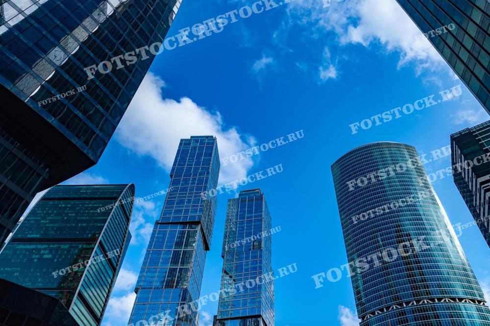 Эта фотография демонстрирует динамичный ракурс небоскрёбов делового центра Москва-Сити. Стеклянные фасады зданий отражают ясное голубое небо и облака, создавая впечатление открытости и высоты. Композиция подчеркивает современный архитектурный стиль и технологичность, характерные для этого района Москвы. Фотография может быть использована в публикациях, посвящённых современной архитектуре, статьях о градостроительстве и в материалах, иллюстрирующих развитие городских пространств.