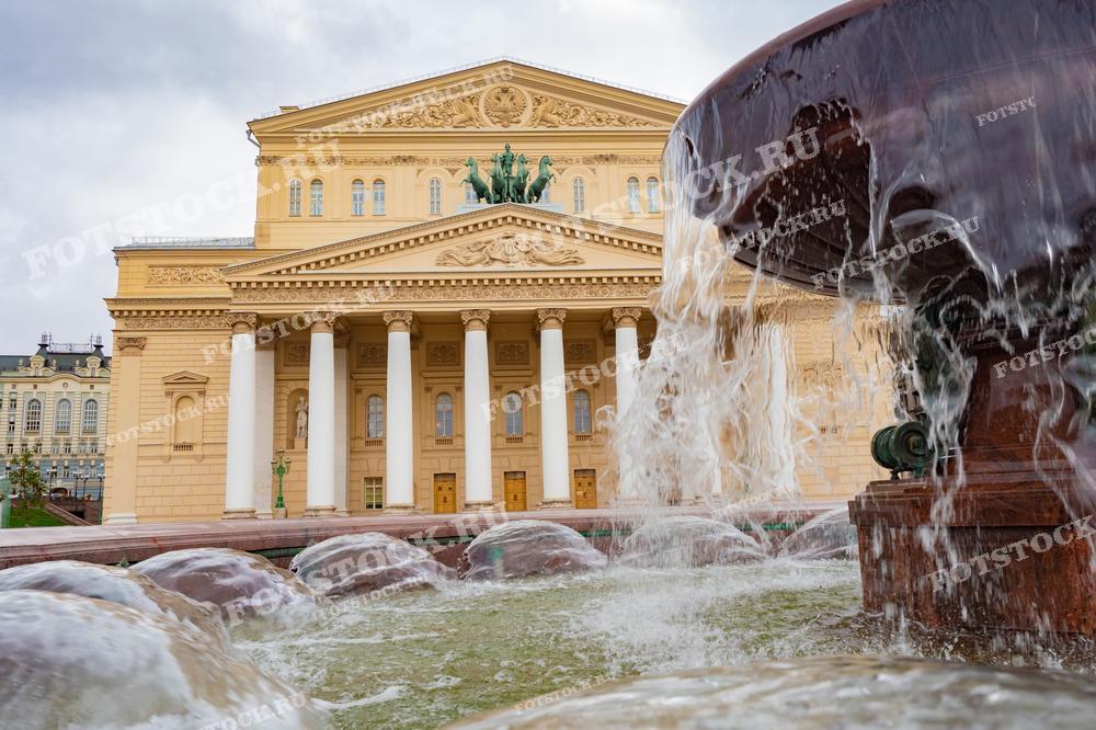 На фотографии изображен Большой театр в Москве, перед которым находится фонтан. Вода из фонтана подчеркивает величественный вид классического фасада театра с колоннами и скульптурами.