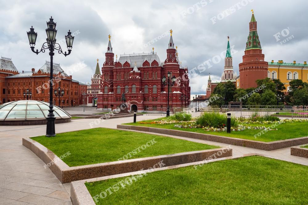 На фотографии изображена площадь в центре Москвы. В центре композиции находится здание Государственного исторического музея с его характерным красным фасадом. Справа видны Кремлёвская стена и башни, а также часть здания Оружейной палаты. Перед музеем благоустроенные зелёные газоны и цветочные клумбы подчёркивают уют и красоту городской среды.
