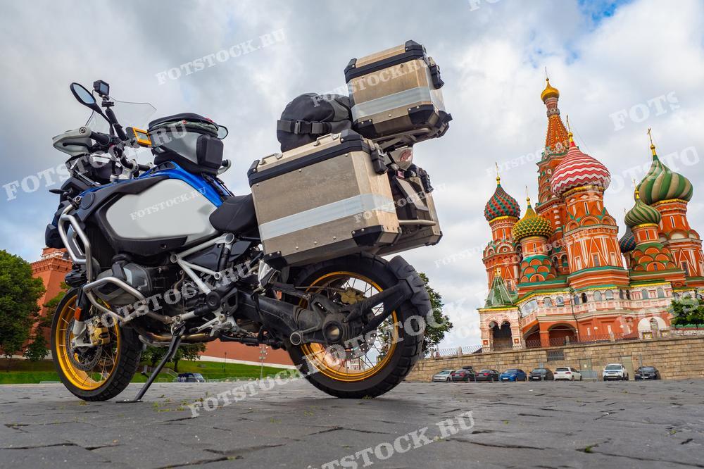 На фотографии изображён туристический мотоцикл, припаркованный на Красной площади перед Собором Василия Блаженного. Контраст между современным транспортом и исторической архитектурой подчеркивает уникальную атмосферу Москвы, где встречаются прошлое и настоящее. Собор с его яркими куполами является одним из самых узнаваемых символов России.