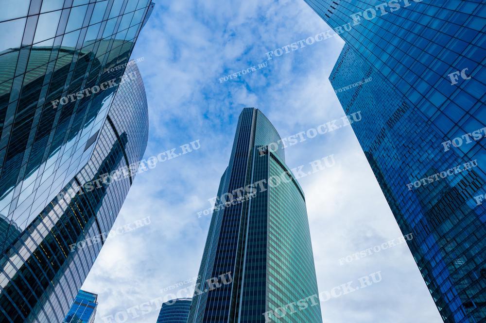 На фотографии представлены современные небоскребы делового района Москва-Сити, вид снизу вверх. Стеклянные фасады зданий отражают небо, создавая эффект объёмности и пространственной глубины. Эти здания являются символом современного экономического и архитектурного развития Москвы. Фотография может использоваться в архитектурных обзорах, публикациях о градостроительстве и в материалах, посвященных современным технологиям в архитектуре.