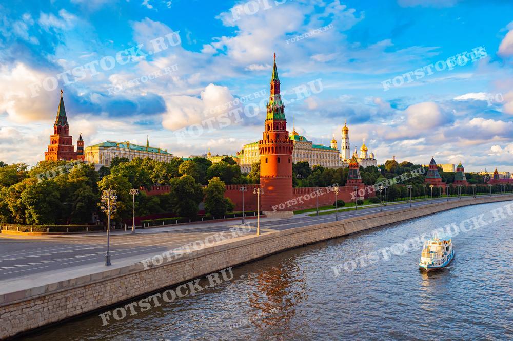 На фотографии запечатлен знаменитый вид на Кремль и Москву-реку. По реке плавает туристический кораблик, добавляя живописности этой городской сцене. Фотография идеально подходит для туристических брошюр или статей, освещающих красоту и историческое значение Москвы.
