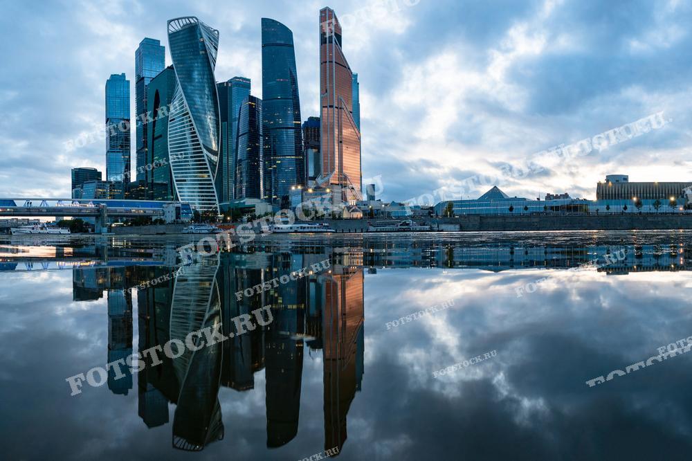 На фотографии показан деловой центр Москва-сити на закате, отражающийся в водах Москва-реки. Небоскребы создают впечатляющую вечернюю панораму современной Москвы.