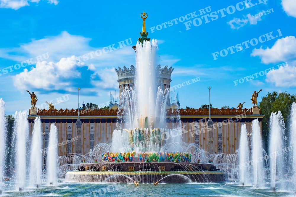 На фотографии изображен фонтан "Каменный цветок" на ВДНХ в Москве. На заднем плане виден павильон с характерной советской архитектурой.