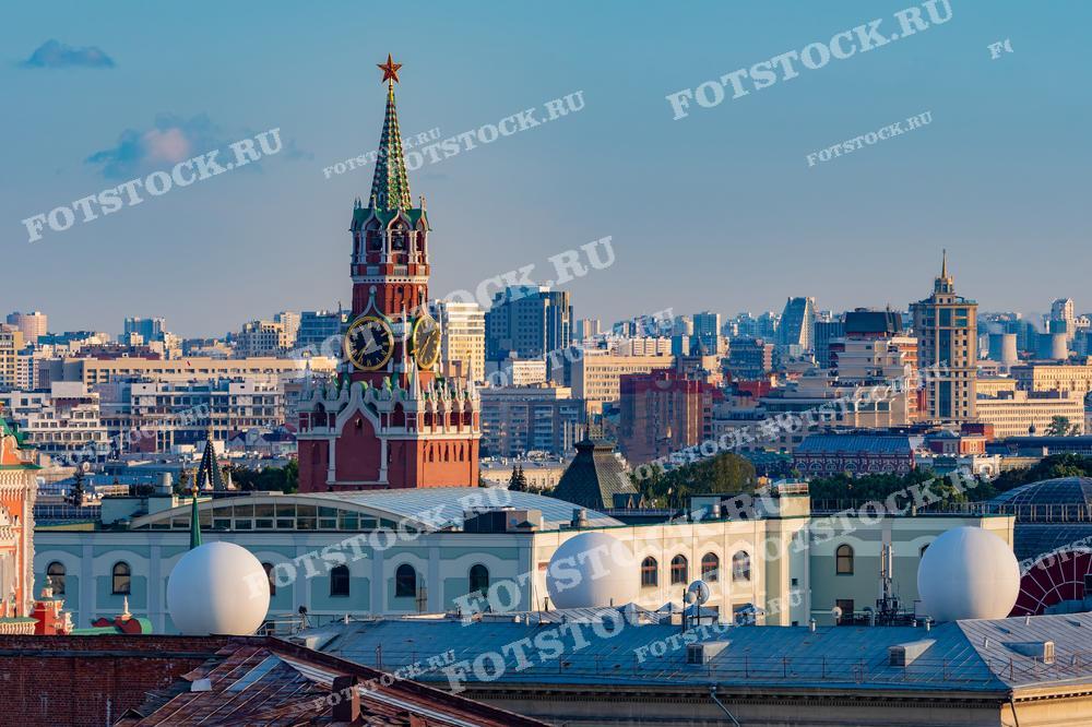 На фотографии изображена Спасская башня Кремля, одна из самых известных и символичных достопримечательностей Москвы. Виден исторический центр города с его уникальной архитектурой. Летний день подчеркивает красоту и величие московского Кремля. На заднем плане можно увидеть современные здания, что создаёт контраст между историей и современностью. Спасская башня с часами является одним из главных символов России.