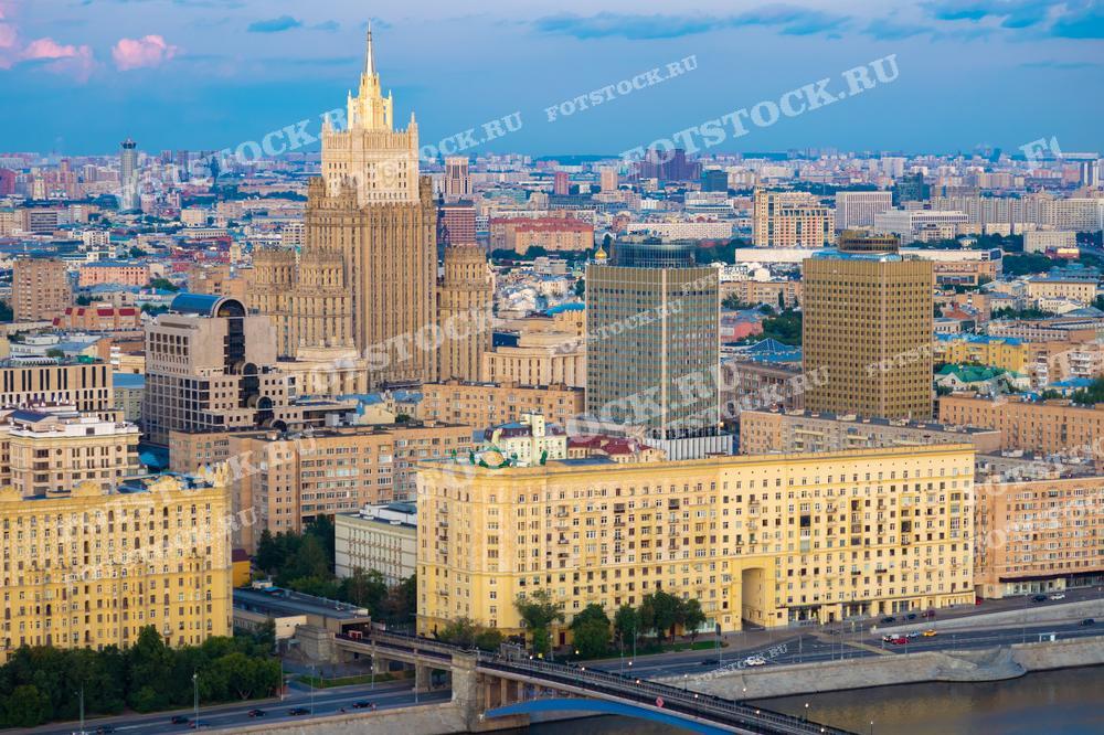 Фотография показывает панорамный вид на Москву, снятый с дрона. В центре кадра видна одна из сталинских высоток - здание Министерства иностранных дел, а также здания на набережной реки Москвы.