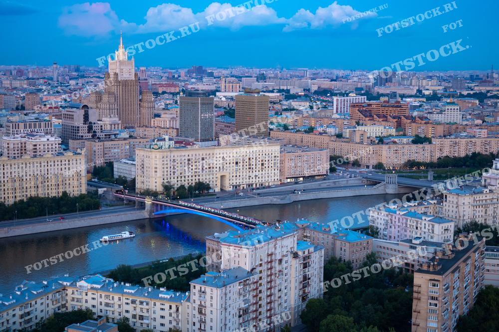 Фотография показывает панорамный вид на Москву, снятый с высоты. Видны набережная реки Москвы и Смоленский метромост. Также над крышами возвышается сталинская высотка - здание Министерства иностранных дел.