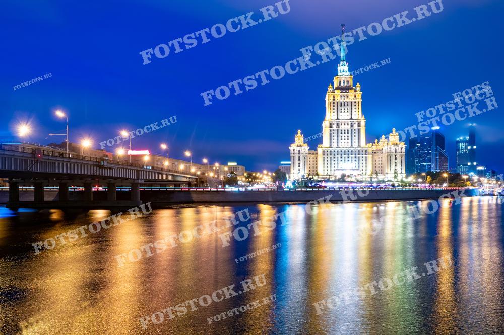 Фотография ночной Москвы с видом на сталинскую высотку и мост через реку Москву. Подходит для использования в материалах о ночной жизни города, архитектуре Москвы и городской инфраструктуре.