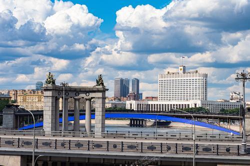 На фотографии запечатлён вид на Москву в день, когда небо покрыто облаками. Видна столица России с её правительственным зданием и мостами через Москву-реку, включая Бородинский мост с каменным аркой. Фотография иллюстрирует архитектуру Москвы и её неповторимый облик. Это изображение может использоваться в туристических брошюрах, книгах о Москве, а также в статьях о городской архитектуре и туризме.