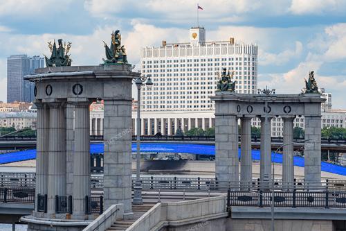 На фотографии запечатлен вид на Московские мосты, арки Бородинского моста и здание российского правительства с белыми стенами и флагом. Эта композиция иллюстрирует городскую архитектуру Москвы и её важные исторические и политические символы. Фотография может быть использована в различных контекстах, включая туристические путеводители по Москве, презентации о российской столице, а также статьи о городской инфраструктуре и политической жизни.