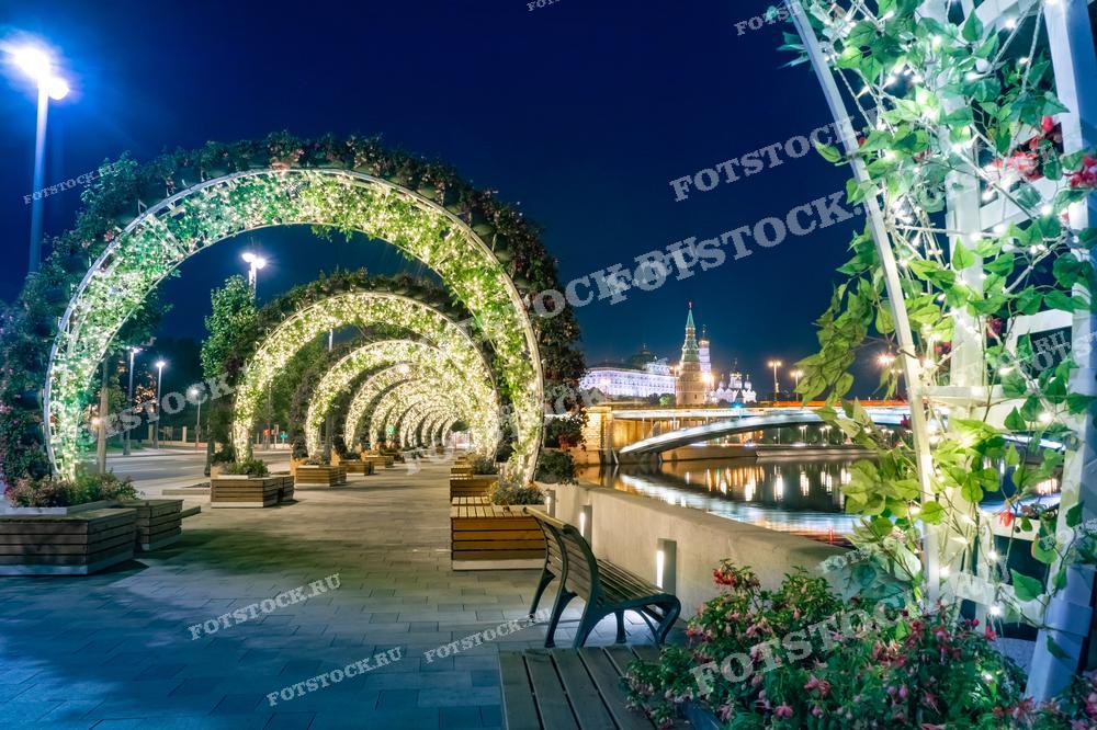 На фотографии изображена ночная набережная в Москве с видами на Кремль. Освещенные арки создают волшебную атмосферу, подчеркивая красоту и спокойствие этого места в ночное время.