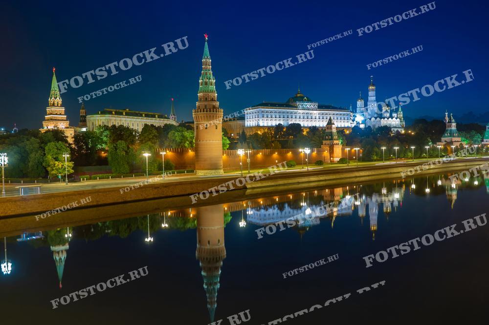 На фотографии изображен ночной вид на Кремль и Москва-реку. Яркие огни Кремля освещают башни и стены, создавая впечатляющие отражения в спокойной воде реки. Ночная атмосфера подчеркивает величие и красоту исторического центра Москвы.