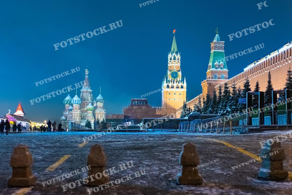 На фотографии представлен зимний вечерний вид Красной площади в Москве. В кадре видны Спасская башня Кремля и собор Василия Блаженного, освещенные в ночной темноте. Эта сцена подчеркивает величие российской архитектуры и историческое значение места. Фотография идеально подходит для туристических проспектов, исторических статей, учебных материалов и публикаций о культурных достопримечательностях Москвы.