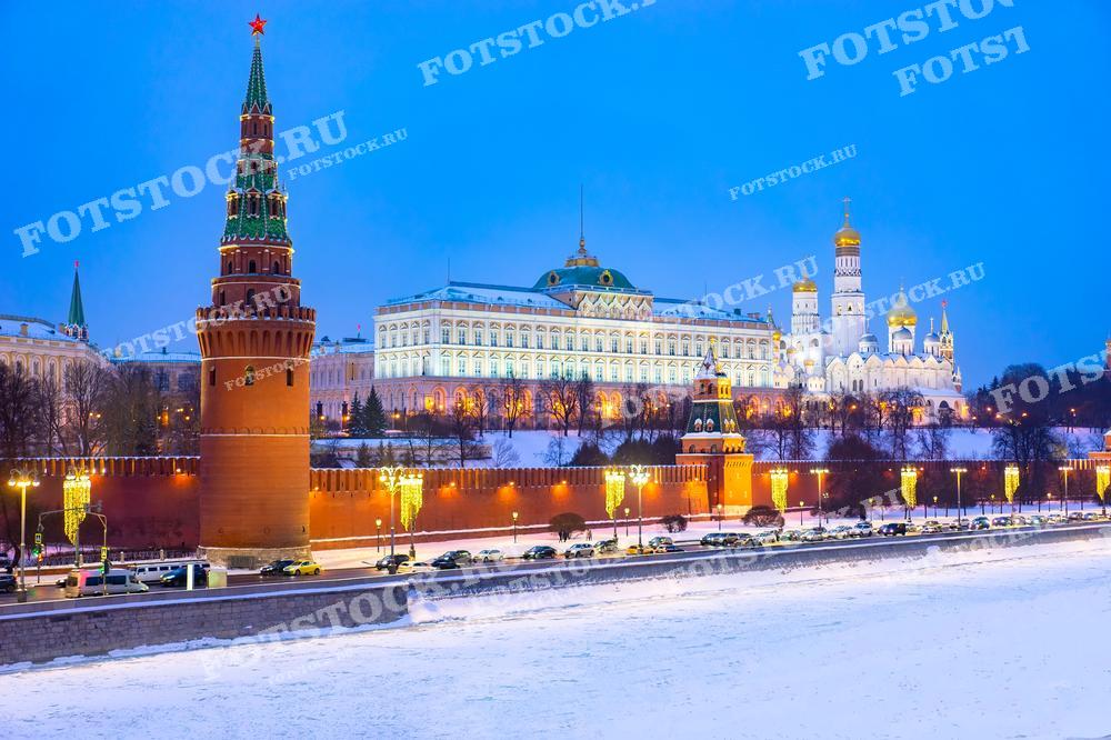 На фотографии изображён Московский Кремль, освещенный и украшенный к Рождеству. Знаменитая красная стена Кремля, Боровицкая башня и соборные здания сияют разноцветными огнями, что создает торжественную и праздничную атмосферу. Дорожки Кремля покрыты снегом, а фонари вдоль дороги добавляют уют и тепло этой зимней сцене. Это изображение идеально подходит для использования в материалах, посвященных рождественским и новогодним праздникам, а также в туристических публикациях о Москве.