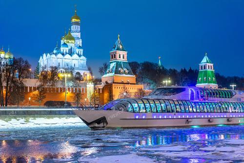 На этой фотографии запечатлен Московский Кремль зимним вечером, обрамленный вечерним освещением и расположенный у берегов реки Москвы. По реке движется экскурсионный теплоход. В атмосфере Рождества и Нового года город оживает, а Кремлевская стена становится фоном для праздничной иллюминации. Этот снимок идеально передает атмосферу зимних праздников в России и может быть использован для туристических брошюр, календарей, открыток или статей о рождественской Москве. Также он подходит для рекламы тематических туров по Москве и круизов по реке Москве.