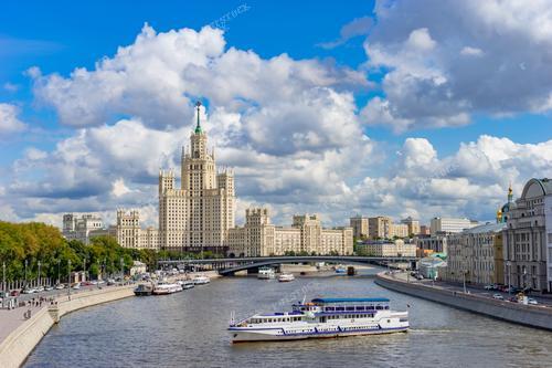 На этой фотографии запечатлена панорама Москвы, столицы Российской Федерации, с рекой Москвой и катерами, предлагающими туристические поездки по реке. Высотное здание на набережной дополняет городскую сцену. Этот снимок идеально подойдет для использования в туристических брошюрах, рекламе тематических экскурсий, календарях или статьях о достопримечательностях Москвы. Он иллюстрирует живописные виды столичной архитектуры и речного движения, оживляющего улицы города в теплое летнее время.