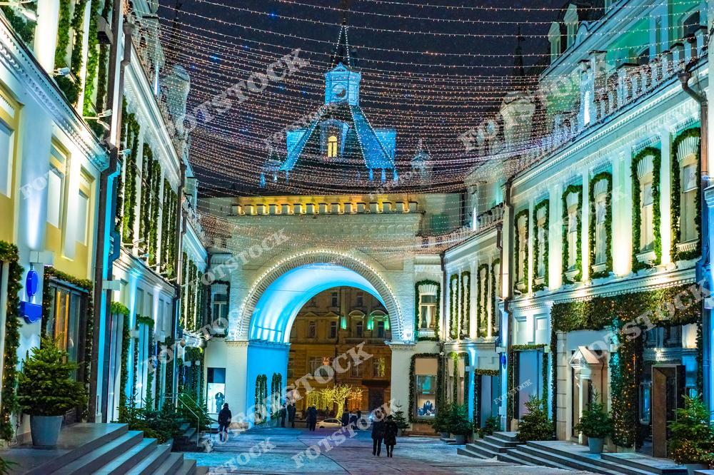 На фото запечатлены рождественские украшения Москвы в период новогодних праздников. Гирлянды, создающие яркую атмосферу, висят над пешеходной улицей, придавая столице особый праздничный вид. Рождественские гуляния и праздничное оформление улиц делают Москву особенно привлекательной в зимний период. Город, украшенный огнями, символизирует радость и волшебство, которые охватывают Москву в канун Рождества и Нового года, становясь важной частью культурной жизни столицы.