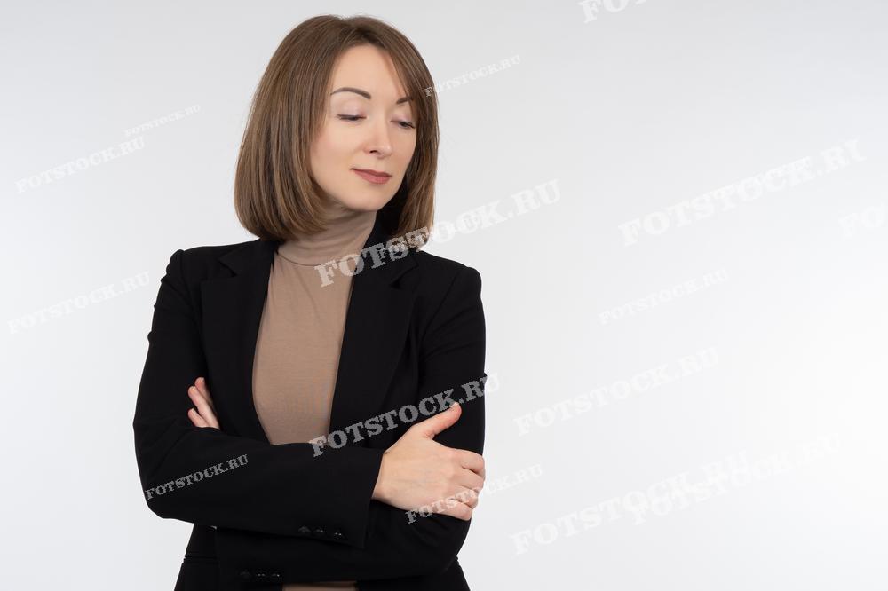 Фотография женщины в деловом костюме, скрестившей руки на груди, на светлом фоне. Снимок подчеркивает уверенность, стиль и профессионализм современной деловой женщины.