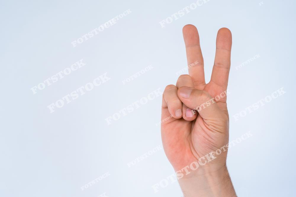 На фотографии изображена человеческая рука, показывающая жест "V" или "знак победы". Светлый фон создает атмосферу легкости и фокусирует внимание на символическом жесте. Сцена передает концепцию мира, успеха и положительных эмоций.