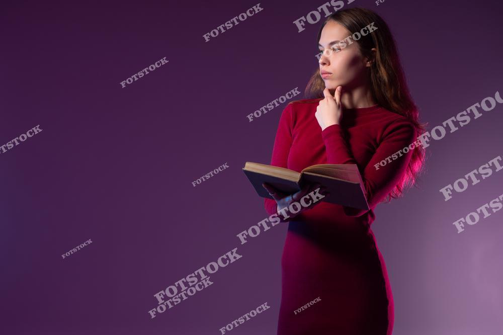 На фотографии изображена женщина в красном платье, держащая книгу в руках. Её задумчивый взгляд и поза подчеркивают процесс размышлений и анализа прочитанного. Фиолетовый фон добавляет глубины и создаёт атмосферу спокойствия и сосредоточенности.