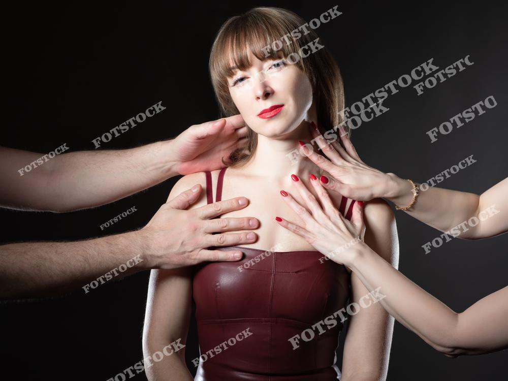 На фотографии изображена женщина, к которой протянуты несколько рук, касающихся ее шеи и плеч. Ее лицо выражает смесь смирения и напряжения, что передает чувство давления и вторжения в личное пространство. Снимок символизирует нарушение границ и воздействие внешнего контроля.